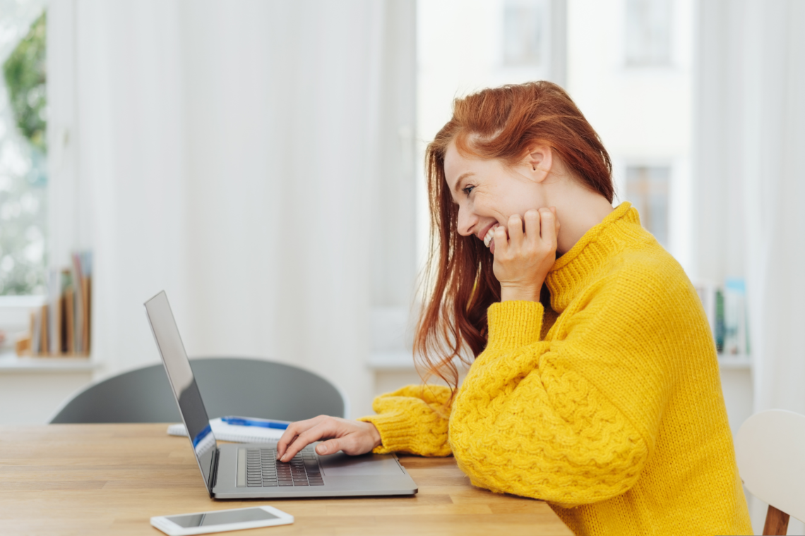 Young cheerful red-haired woman in yellow sweater using laptop to search for sperm donors